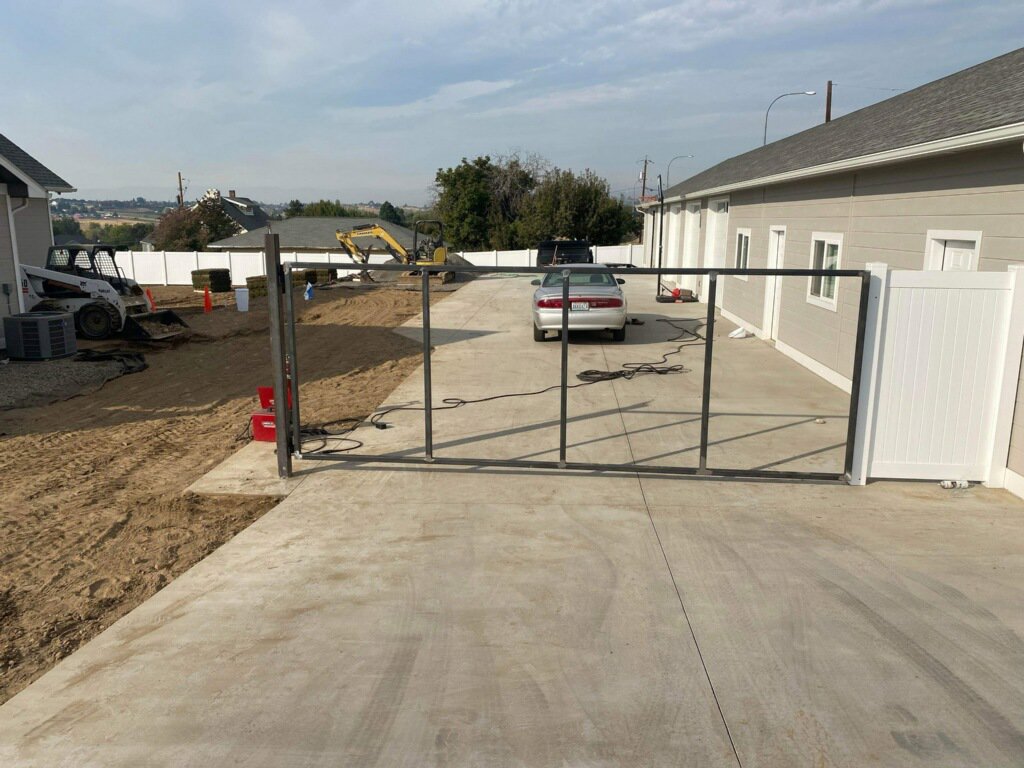 A metal gate frame being installed next to a white vinyl fence by Integrity Gates and Fencing in Yakima, WA