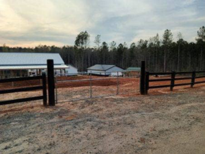 A newly installed metal gate within a black wooden fence by Almaraz & Sons LLC in Macon, GA.
