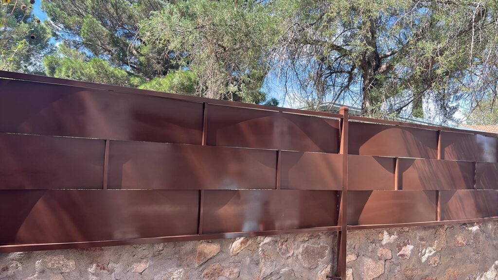A metal privacy fence with a stone wall base by Iron Man Exteriors in Las Cruces, NM.