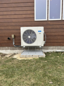 An outdoor Midea heat pump unit installed next to a house by BRY Heat and Air in Elgin, MN