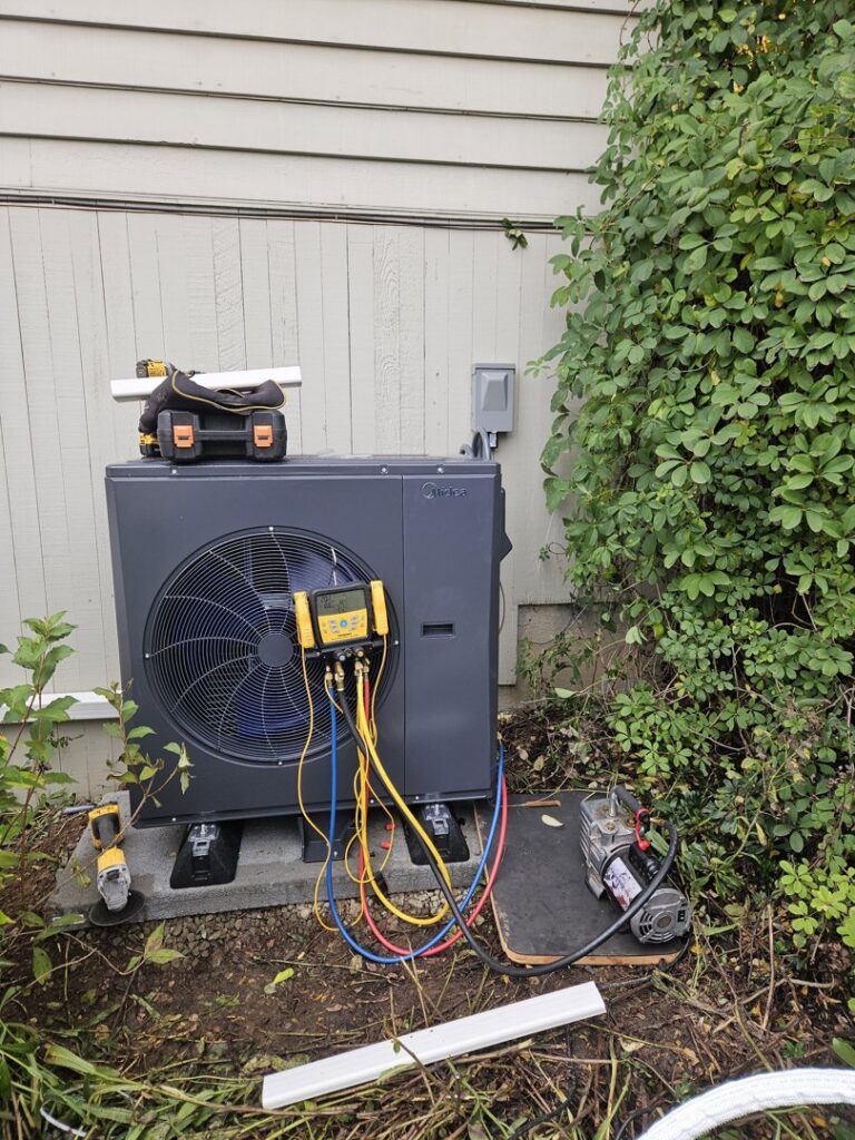 A Midea heat pump unit undergoing installation or service with gauges and a vacuum pump by Conrad Heating and Cooling in Beaverton, OR.