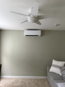 A mini-split AC unit installed on a green wall in a living room by Precision Heating and Gas Service in Derry, NH