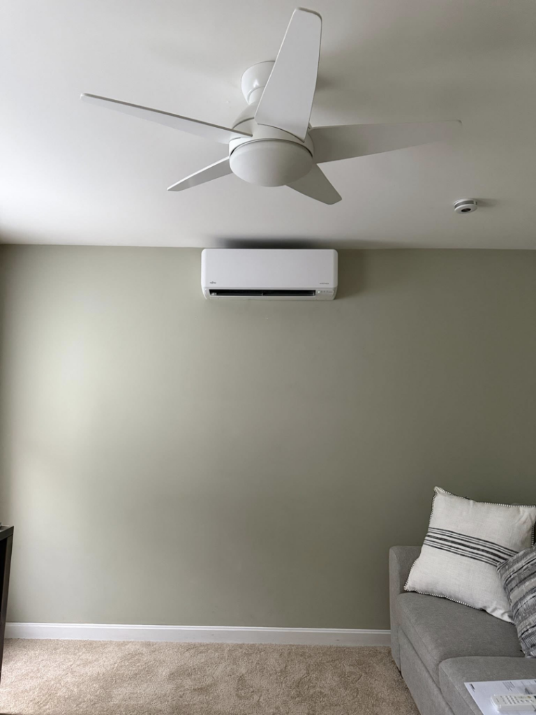 A mini-split AC unit installed on a green wall in a living room by Precision Heating and Gas Service in Derry, NH