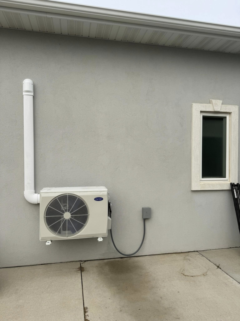 An outdoor Carrier mini-split air conditioning unit installed on a building wall by Golden Heating and Air LLC in Arvada, CO.