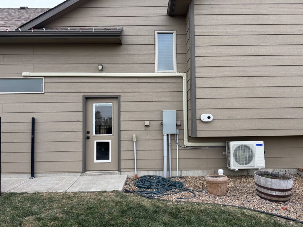 A mini-split AC unit and exterior piping installed on the side of a home by Great Plains Heating & Air in Goddard, KS.