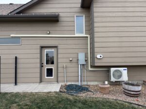 A mini-split AC unit and exterior piping installed on the side of a home by Great Plains Heating & Air in Goddard, KS.