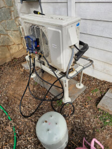 A mini-split AC outdoor unit undergoing refrigerant service with gauges and a tank attached by MasterCraft Mechanical, LLC. in Haslet, TX.