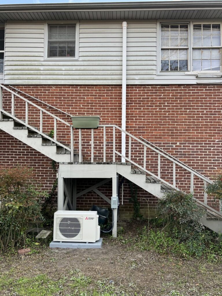 An outdoor mini-split condenser unit professionally installed next to a brick building by Advance Heating & Air, Inc. in Sumter, SC.