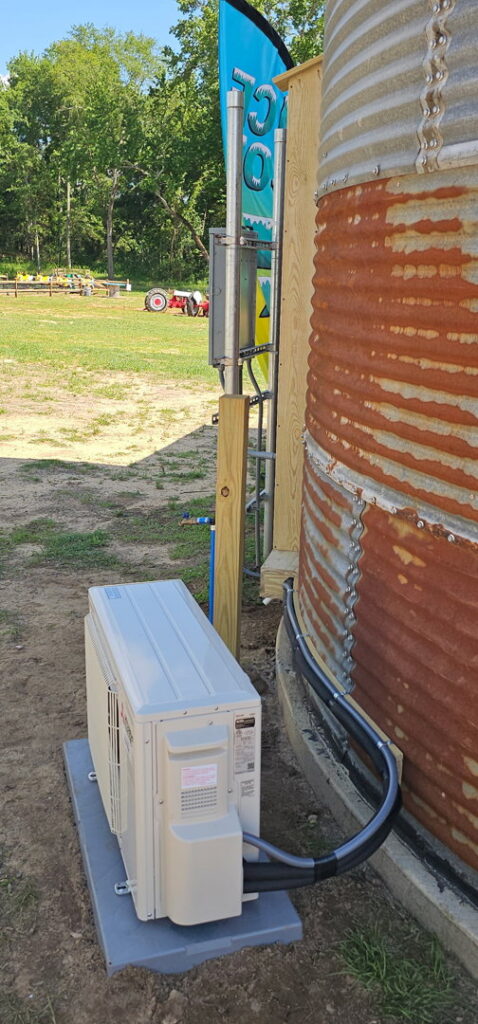 An outdoor mini-split condenser unit installed next to a corrugated metal silo by Advance Heating & Air, Inc. in Sumter, SC.