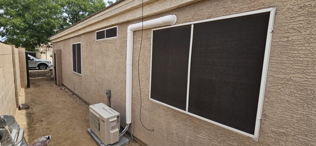 An outdoor mini-split condenser unit with white conduit installed against a residential wall by HoxAir Heating & Cooling in Phoenix, AZ