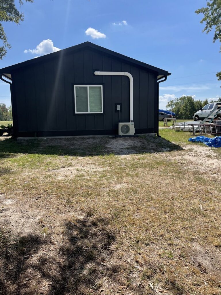 A mini-split outdoor HVAC unit installed on the side of a black building by Luciano's Air Services in Durham, NC.