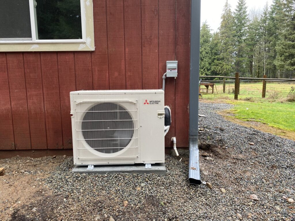 A Mitsubishi Electric mini-split outdoor unit installed against a red residential building by Climate Control Experts HVAC LLC in Federal Way, WA