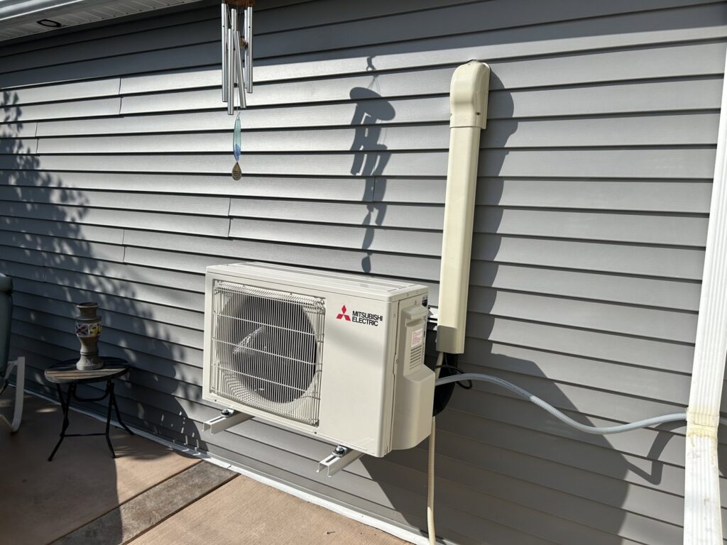 A Mitsubishi Electric outdoor mini-split condenser unit installed on a house wall by Climate Diagnostics in Buffalo, NY.