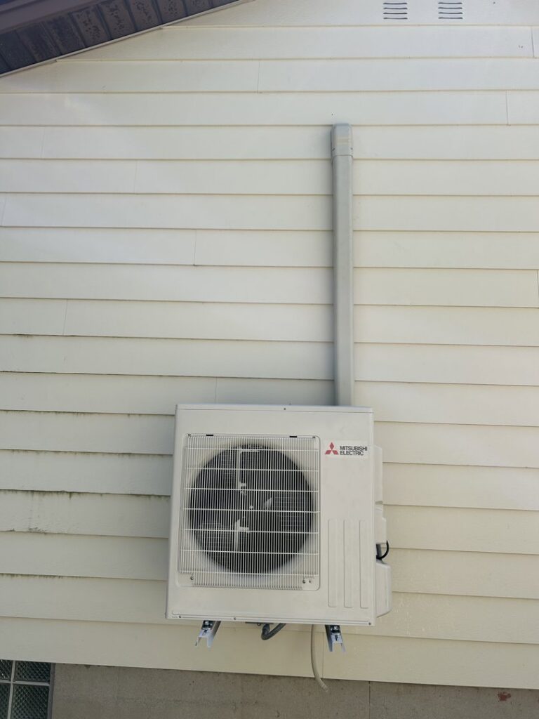 A Mitsubishi Electric outdoor mini-split condenser unit installed on the side of a house by Climate Diagnostics in Buffalo, NY.