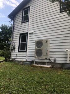 An outdoor Mitsubishi Electric HVAC unit installed on a concrete pad next to a white residential building by Simply Installs Heating & Air Conditioning in Shortsville, NY.