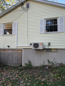 A newly installed Mitsubishi heat pump outdoor unit on the side of a residential building by S&J Heat Pumps in Augusta, ME.