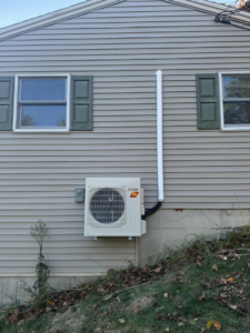 A Mitsubishi heat pump outdoor unit with conduit installed on the exterior of a home by S&J Heat Pumps in Augusta, ME.