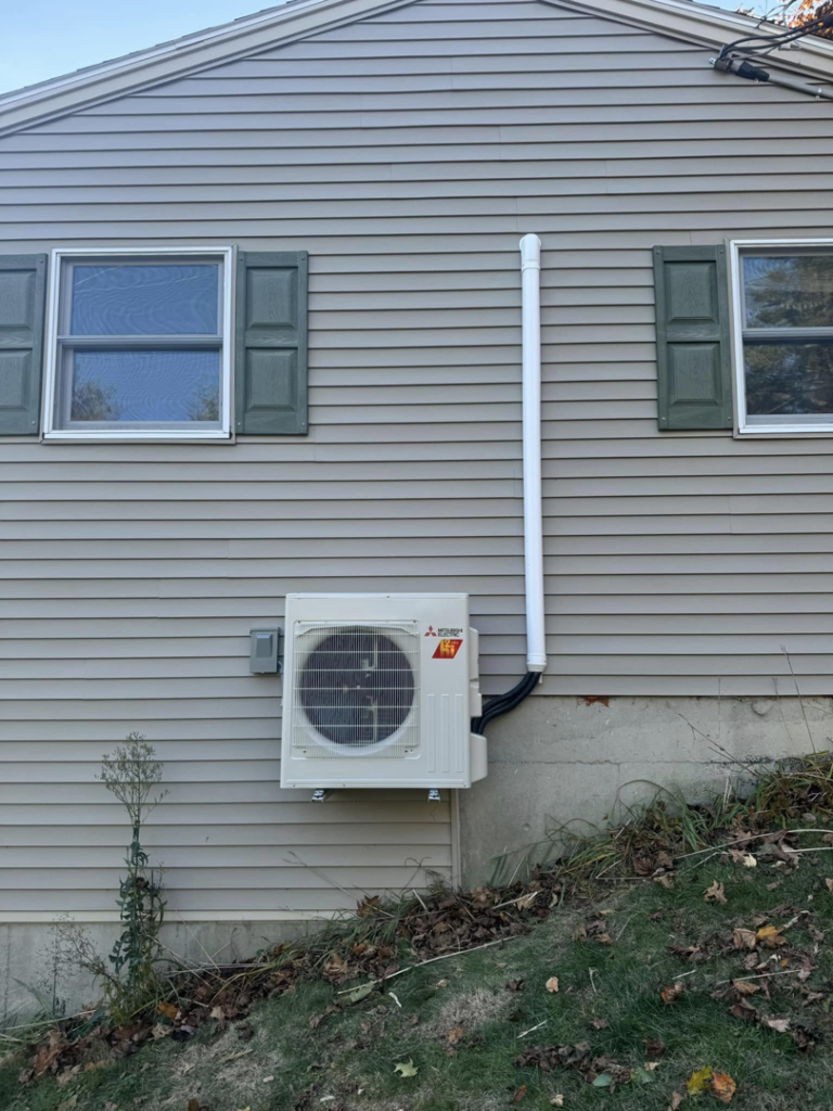 A Mitsubishi heat pump outdoor unit with conduit installed on the exterior of a home by S&J Heat Pumps in Augusta, ME.