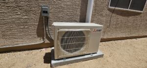 A Mitsubishi Electric mini-split outdoor condenser unit installed against a residential wall by HoxAir Heating & Cooling in Phoenix, AZ