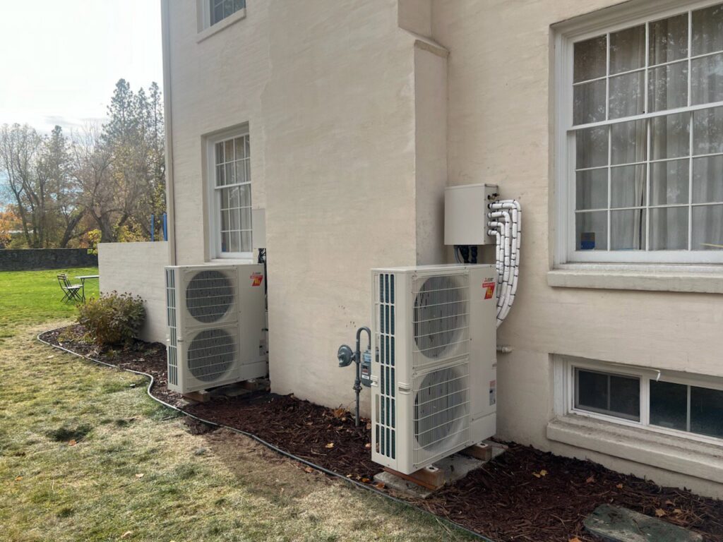 Two Mitsubishi mini-split outdoor condenser units installed on the side of a building by Semenik Hvac/r in Spokane, WA.