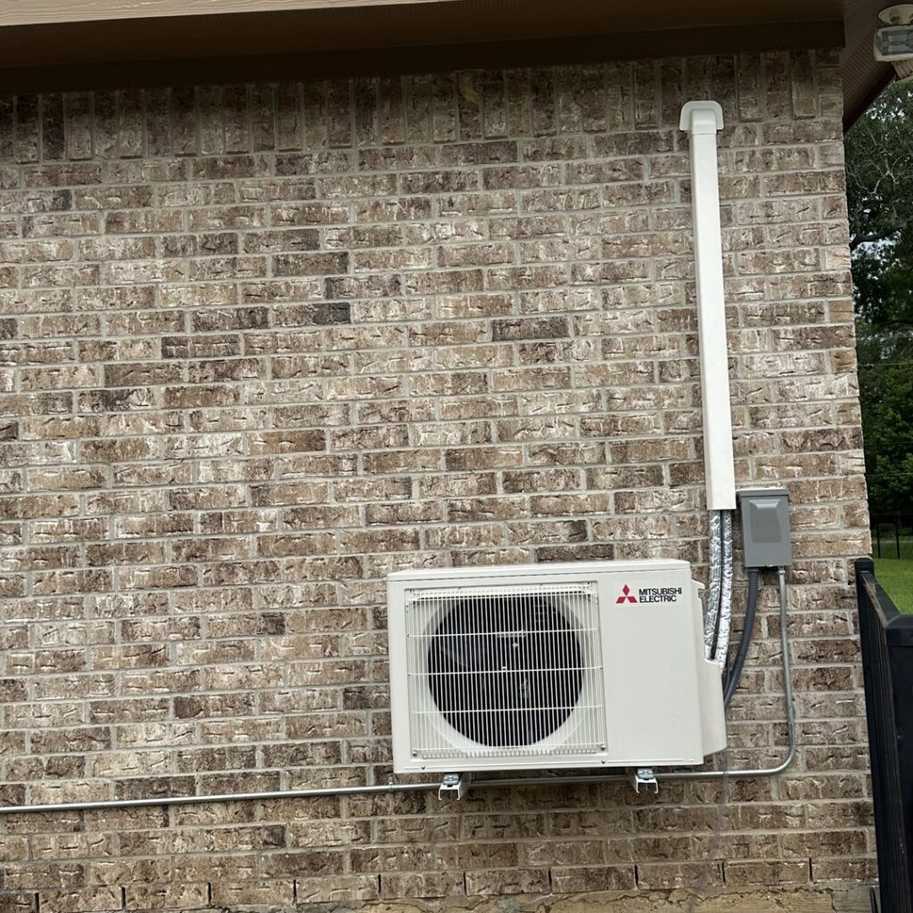 A Mitsubishi Electric mini-split outdoor unit installed on a brick wall by EZ Comfort Air Conditioning & Heating LLC in Humble, TX.