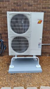 A Mitsubishi multi-split outdoor HVAC unit installed on a stand against a brick wall by Kerley Heating & Cooling in Rock City, IL