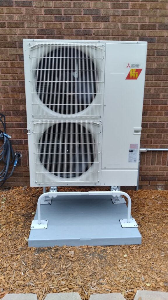 A Mitsubishi multi-split outdoor HVAC unit installed on a stand against a brick wall by Kerley Heating & Cooling in Rock City, IL