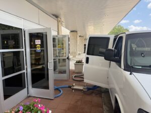 A mobile carpet cleaning setup with hoses extending from a van into a building by Jones Carpet Care LLC in Huntsville, AL.