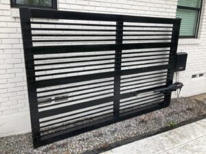 A modern automatic black metal sliding gate installed against a white brick wall by Craftsman Automatic Gates in Dallas, TX.