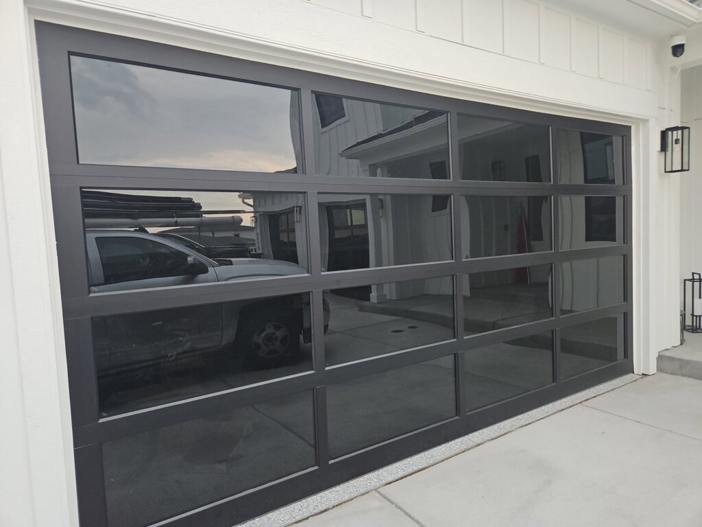 A modern black full-view glass garage door installed on a white contemporary home by Above The Rest Garage Door in Colorado Springs, CO.