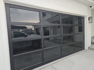 A modern black full-view glass garage door installed on a white contemporary home by Above The Rest Garage Door in Colorado Springs, CO.