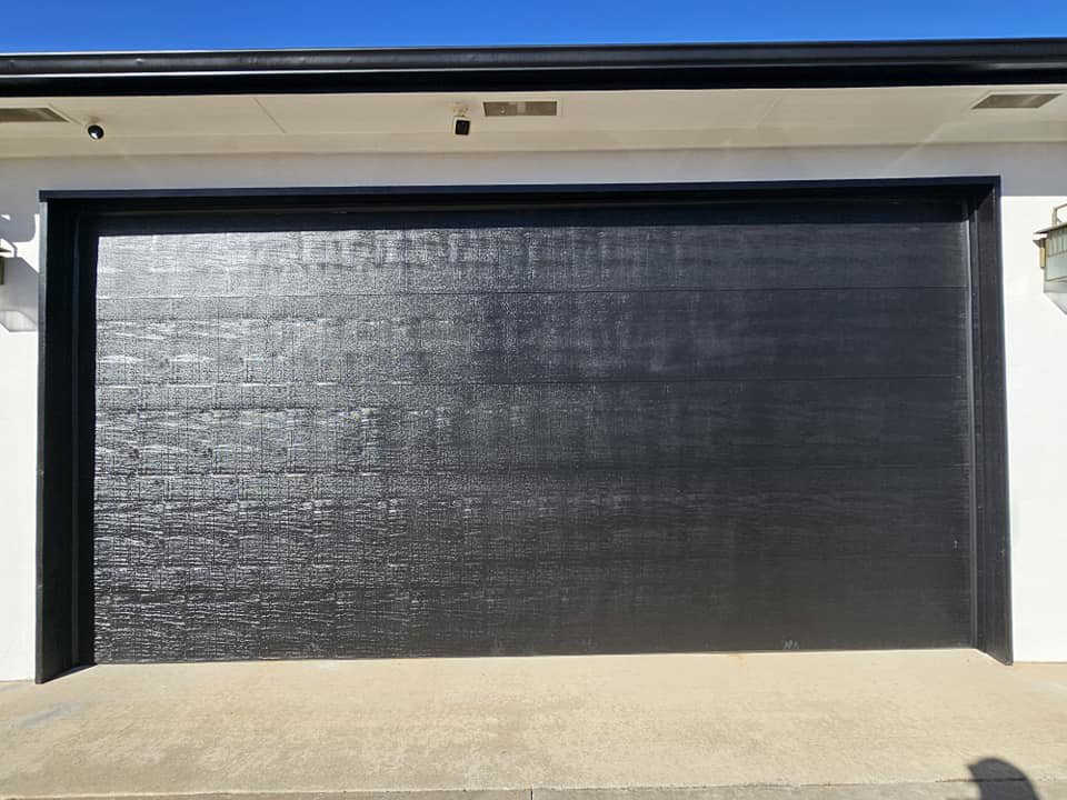 A modern black garage door newly installed on a white house by Total Door Solutions in Yukon, OK