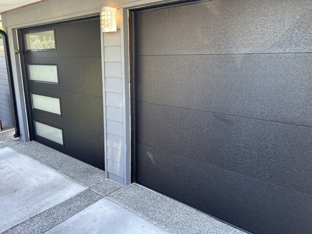 A close-up of two modern black garage doors, one with vertical windows, installed by Coast To Coast Garage Door LLC in Vancouver, WA.
