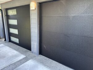 A close-up of two modern black garage doors, one with vertical windows, installed by Coast To Coast Garage Door LLC in Vancouver, WA.