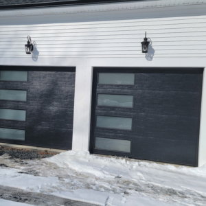 Modern black garage doors with windows installed on a white house exterior, showcasing work by Southcoast Overhead Door & Services in Fall River, MA.