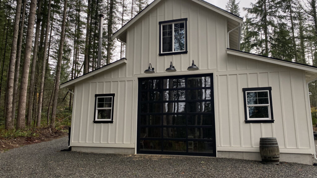 A modern black glass garage door installed on a white barn-style building by Independent Garage Doors LLC in Tacoma, WA.