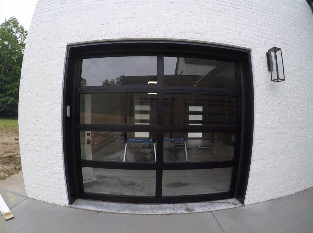 A modern black garage door with glass panels installed on a white brick building by Community Garage Door Services in Louisville, KY.