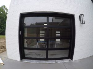A modern black garage door with glass panels installed on a white brick building by Community Garage Door Services in Louisville, KY.
