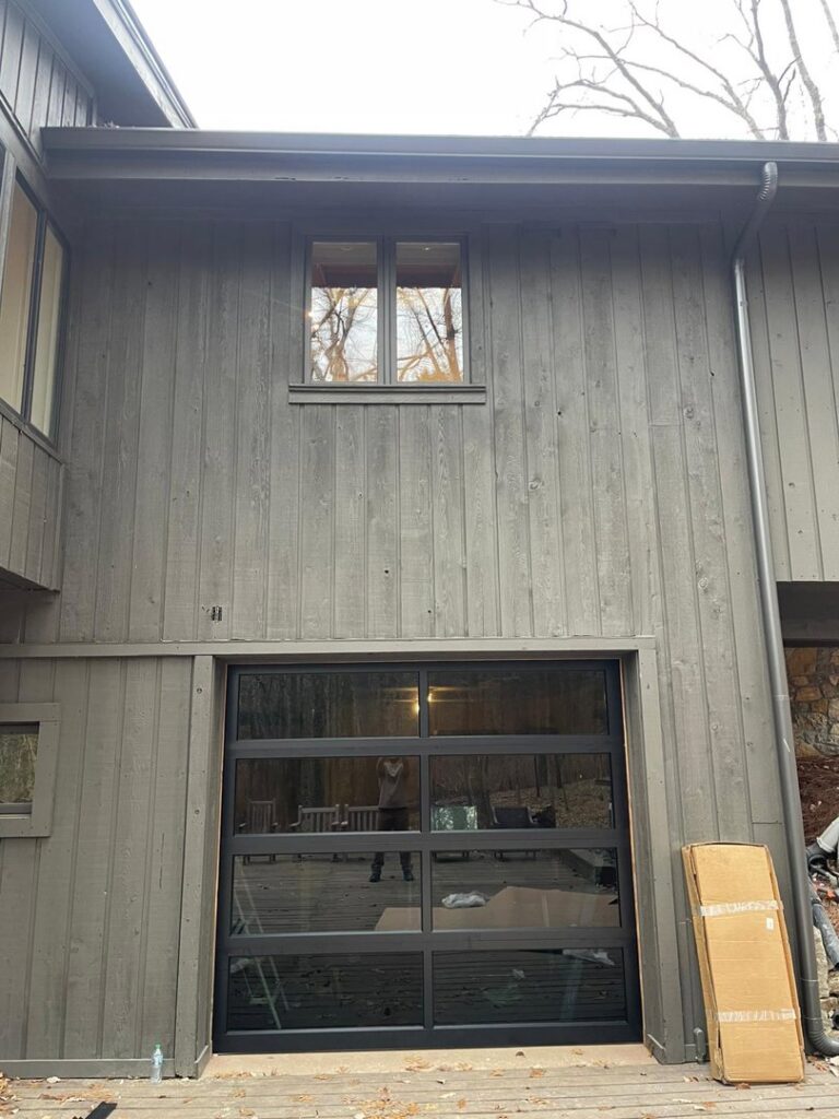 A modern black garage door with full-view glass panels installed on a residential home by Swift Garage Door in Nashville, TN.