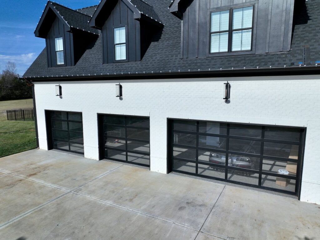 Three modern black glass garage doors installed on a white house by Rose Quality Garage Doors in Murfreesboro, TN