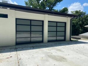 Two modern black garage doors with glass panels installed on a white brick building by Northern Door Company in Murfreesboro, TN