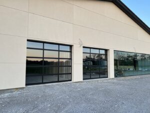 Two modern black garage doors with glass panels installed on a new construction building by Northern Door Company in Murfreesboro, TN