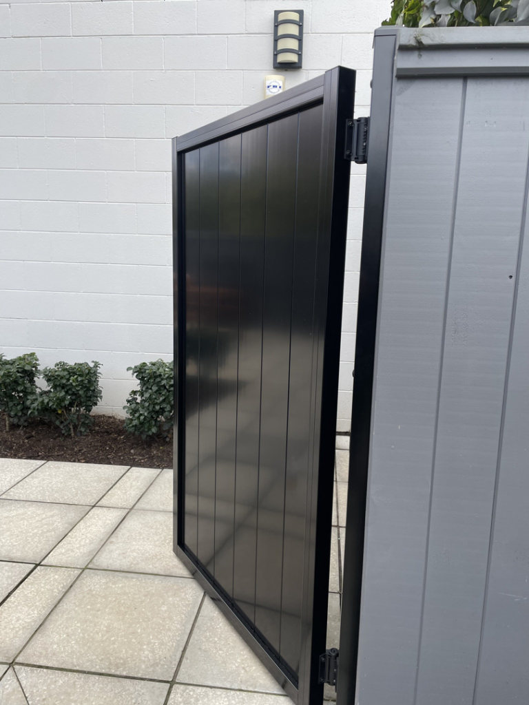 A modern black pedestrian gate installed next to a grey fence panel by Bespoke Gate Fence & Deck in Christchurch, NZ.