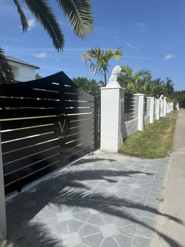 A modern black slat gate with a custom 'V' logo and matching fence installed by A Master Work Corp. in Hialeah, FL.