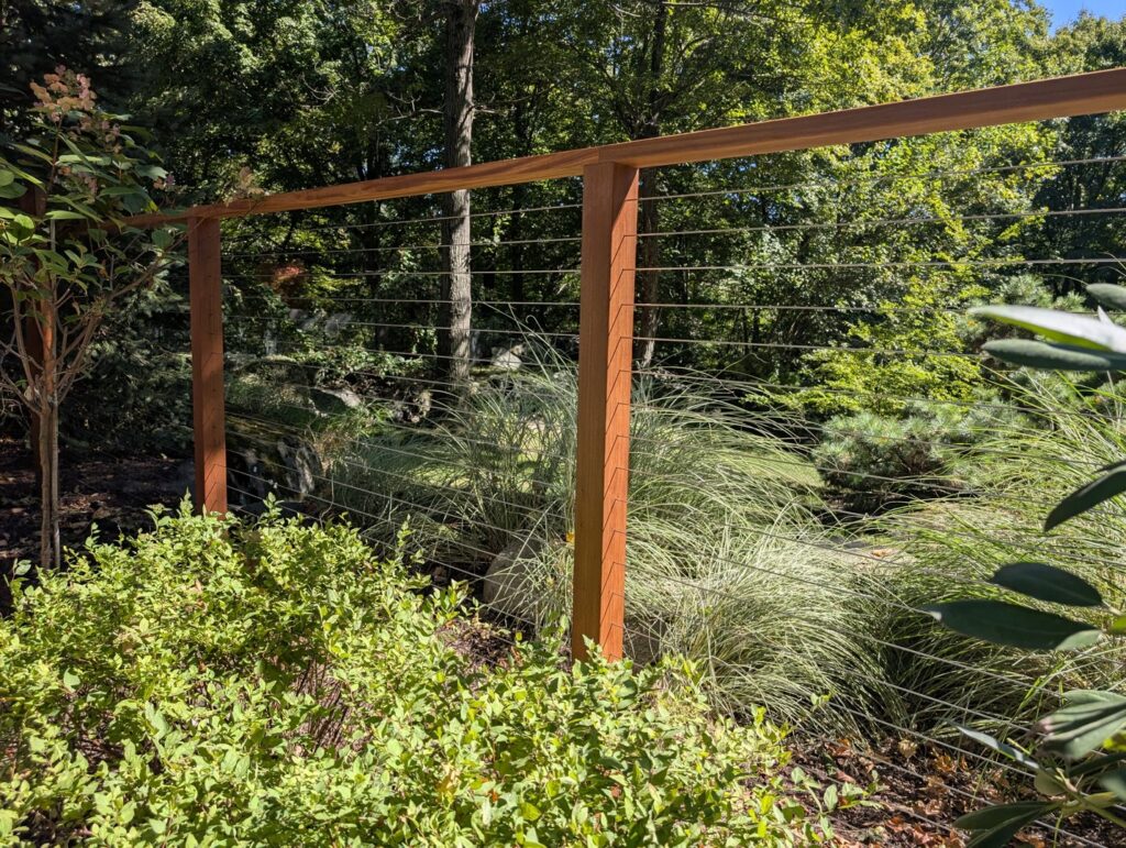A modern cable railing fence with wooden posts in a garden by RP Fencing & Gates in Brewster, NY