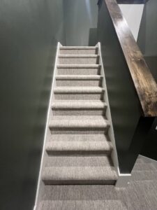 A modern carpeted staircase with dark walls and a wooden handrail by Absolute Floor Covering, Inc in Kentwood, MI.