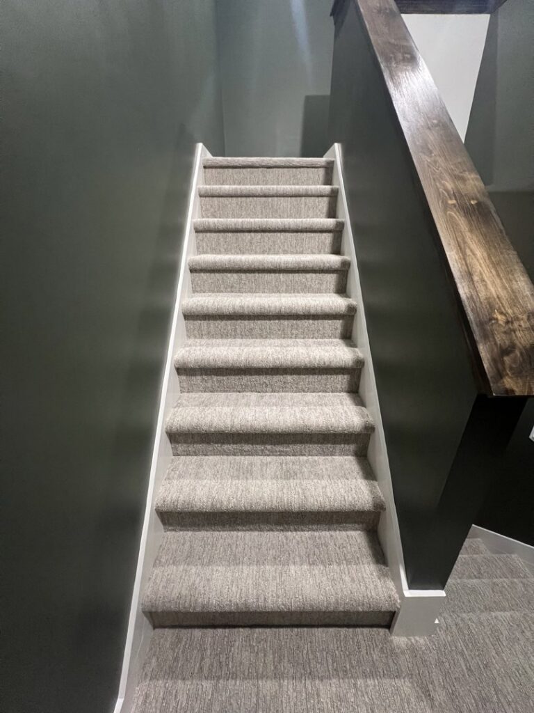 A modern carpeted staircase with dark walls and a wooden handrail by Absolute Floor Covering, Inc in Kentwood, MI.