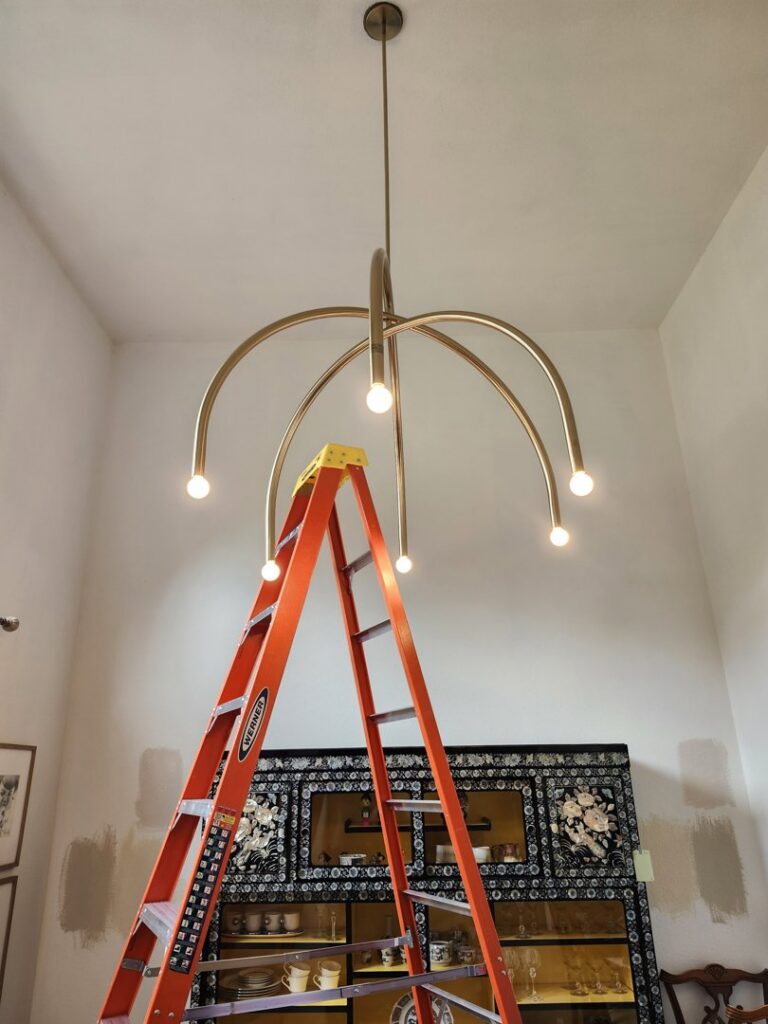 A modern chandelier being installed with a ladder by ABS Electrical Services in Rogers, AR.