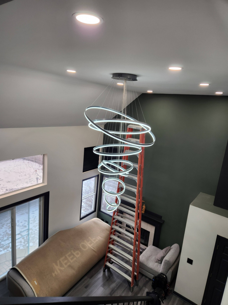 A modern chandelier being installed in a high-ceiling room by Ed's Electrical & Mounting services in Chicago, IL.