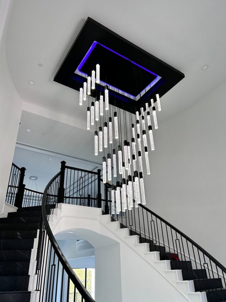 A stunning modern chandelier expertly installed above a grand staircase by Mister Sparky NWA in Springdale, AR.